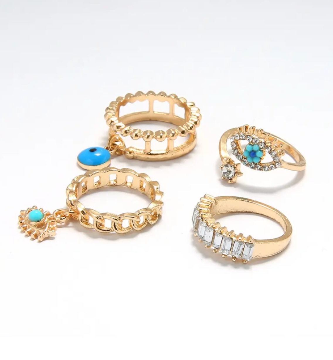 Gold ring stack with blue evil-eye motifs and crystal baguettes on white satin.