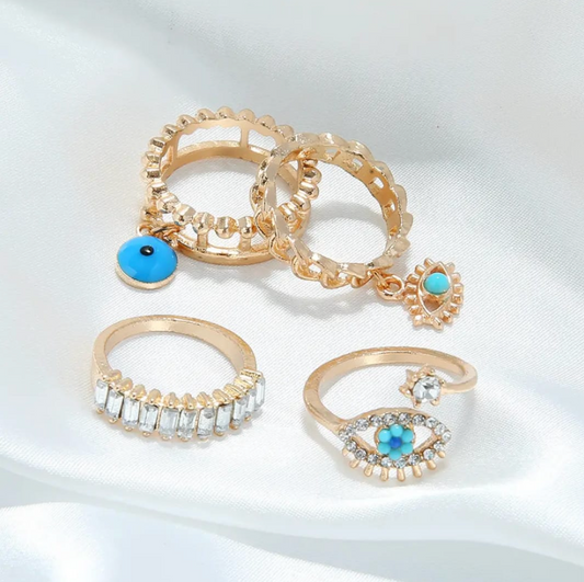 Set of four gold rings: two cutout bands with turquoise evil-eye charms, a baguette CZ band, and an open evil-eye ring.