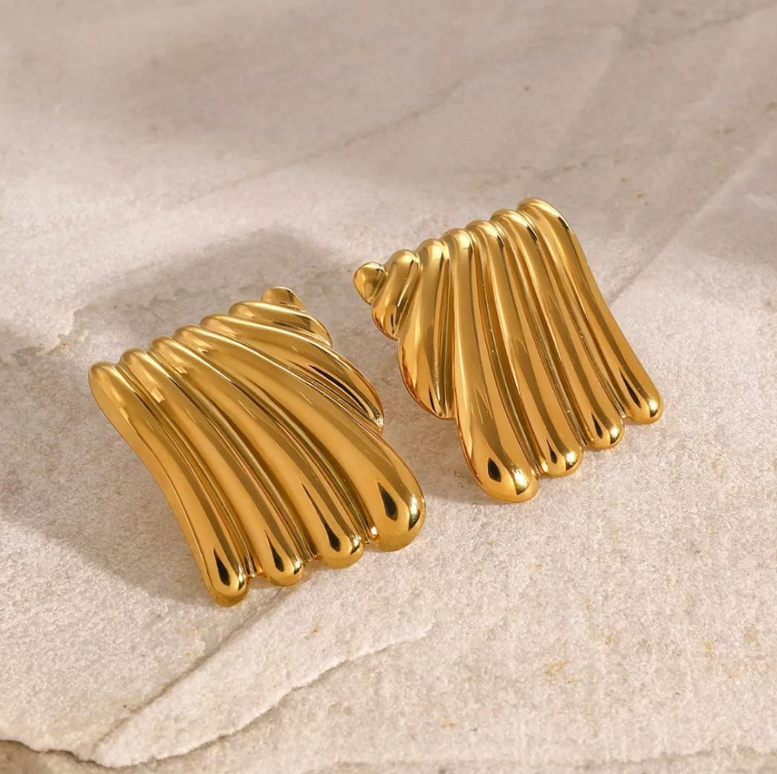 Bold gold plaque earring featuring wavy fluted lines, shown worn on ear.
