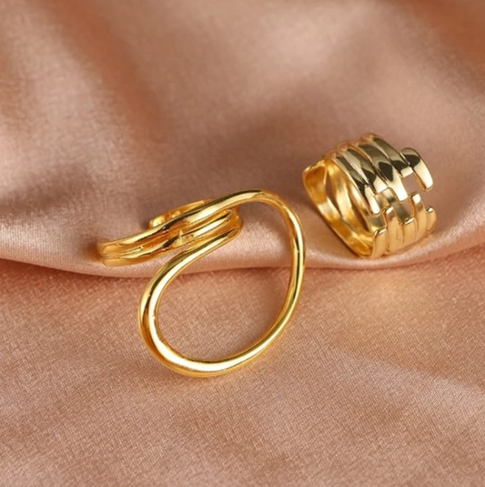 Two gold statement rings on blush satin: sculptural open loop ring and ridged multi-band stack ring.