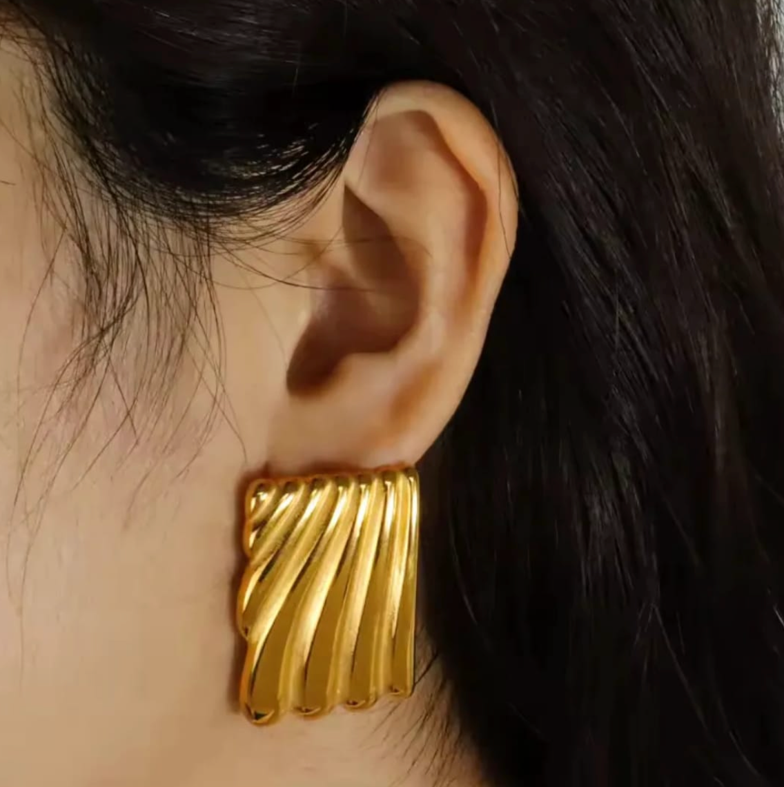 Close-up of a chunky gold rectangle earring with diagonal ridges, worn on ear