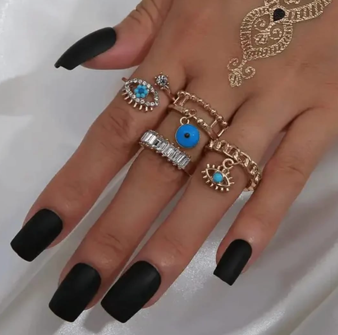 A hand wearing a set of gold-tone rings with evil eye motifs and crystals.
