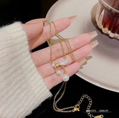 Gold chain necklace with a crystal bow and twin pearl drops, shown in hand with a beige sweater