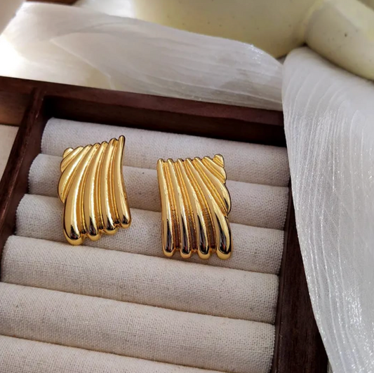 A pair of gold-plated Korean-style earrings with a wave-like design, displayed in a jewelry box.