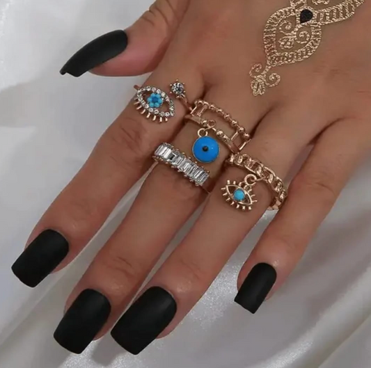 A hand wearing a set of gold-tone rings with evil eye motifs and crystals.
